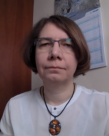Prof. Agnieszka Kwiatkowska ubrana w białą koszulę i wisiorek patrzy w obiektyw, nosi okulary. W tle widać ściany gabinetu.