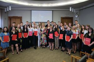 Studenci i studentki UAM zgromadzeni w sali Senatu UAM z dyplomami Społecznika Roku pozują do zdjęcia z prorektor ds. studenckich i kształcenia prof. Joanną Wójcik.