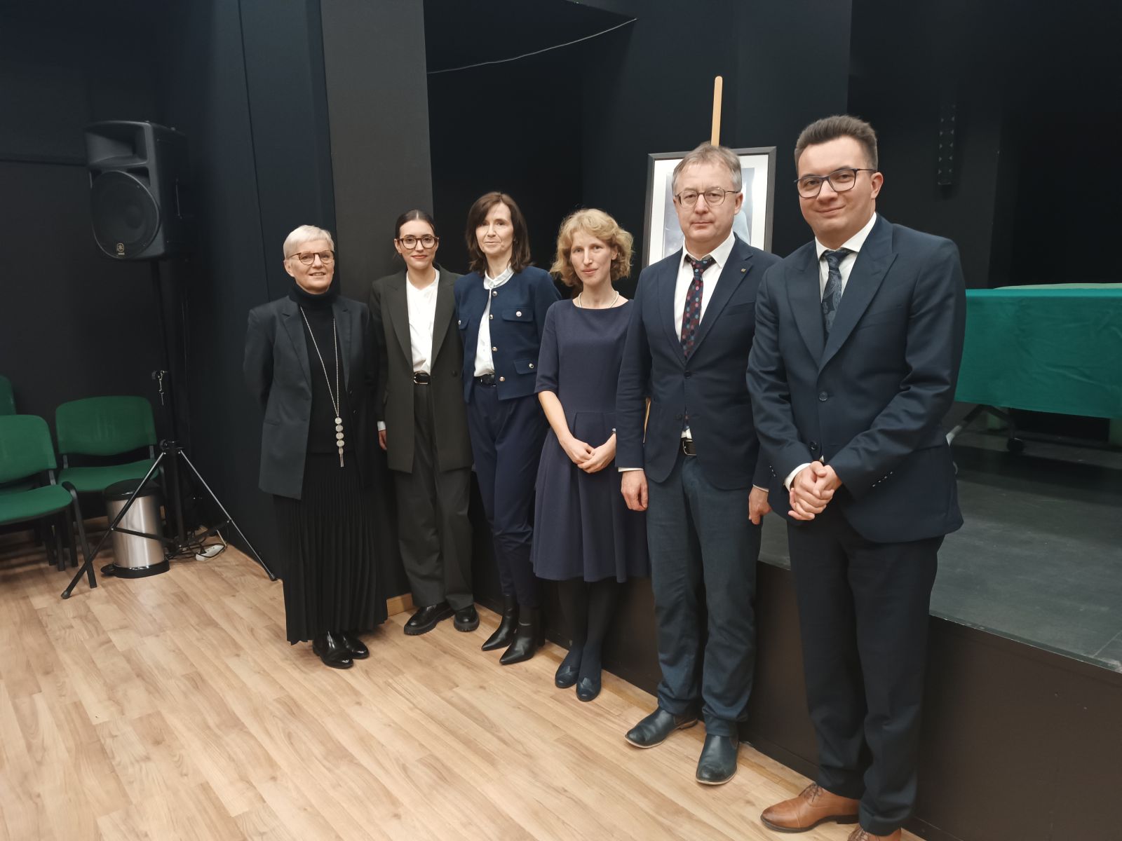 Laureatki tegorocznej edycji konkursu oraz laureat edycji zeszłorocznej stoją wraz prof. Agatą Stankowską-Balcerzan, prof. Elżbietą Winiecką i prof. Tomaszem Mizerkiewiczem na tle sceny z plakatem ze zdjęciem prof. Czesława Zgorzelskiego, pozując z uśmiechem do pamiątkowego zdjęcia.