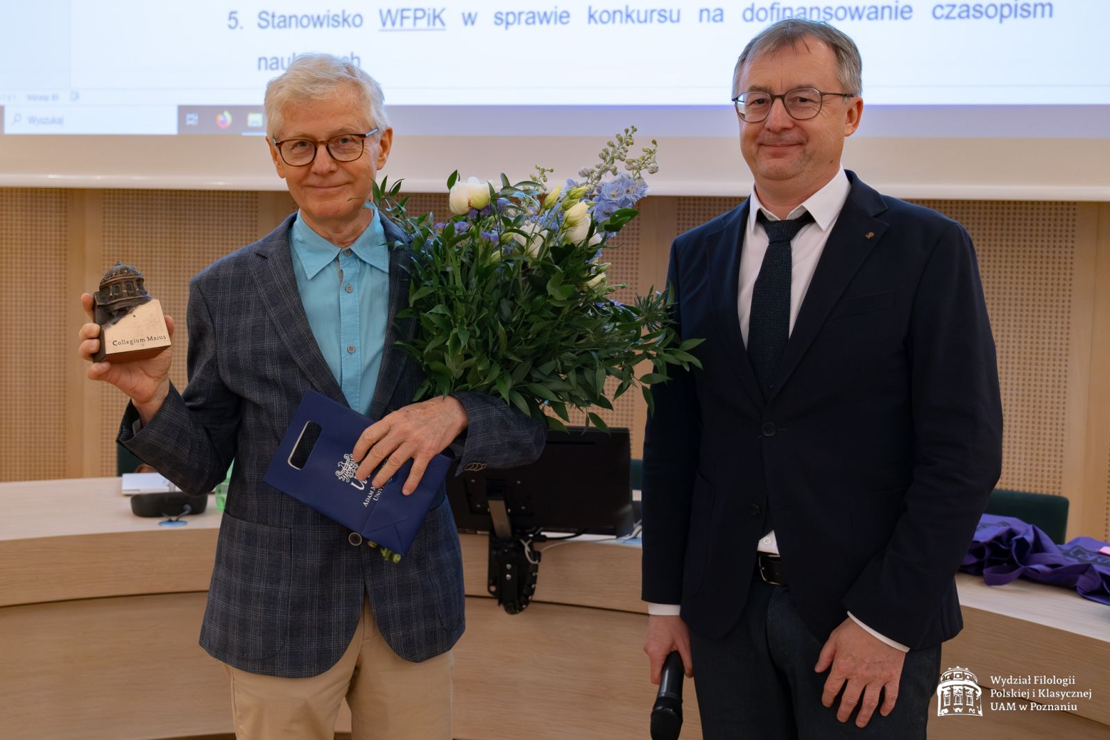 Prof. Przychodniak prezentuje statuetkę Collegium Maius, w drugiej ręce trzyma bukiet kwiatów, obok stoi uśmiechnięty dziekan WFPiK.