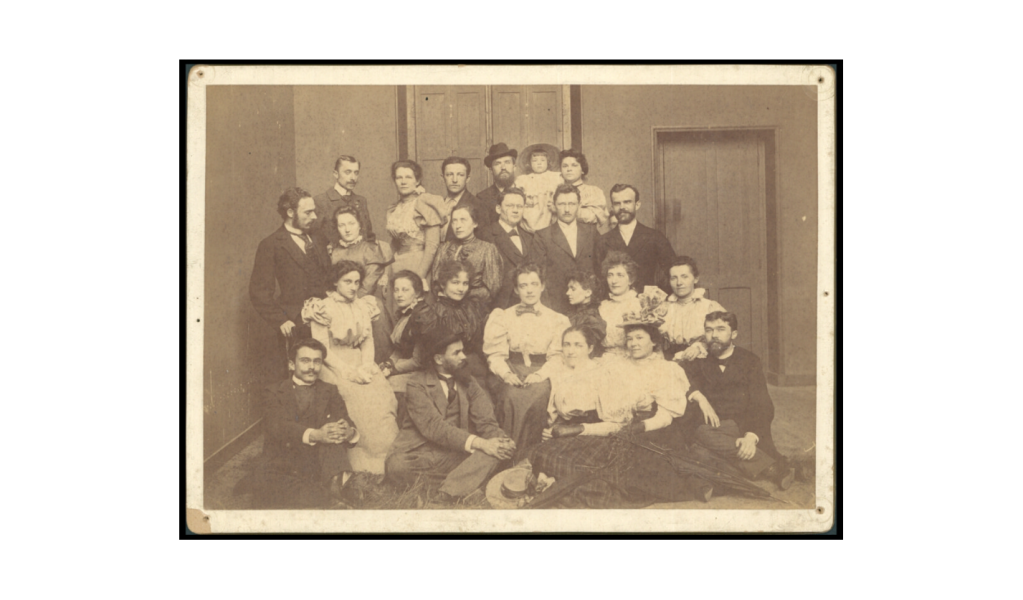 Sepiowe zdjęcie zbiorowe dużej grupy osób, ubranych według mody z końca XIX wieku.