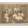 Sepiowe zdjęcie zbiorowe dużej grupy osób, ubranych według mody z końca XIX wieku.