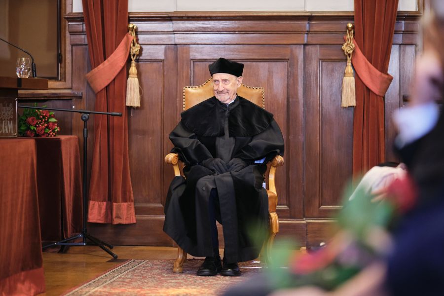 W Auli Lubrańskiego na honorowym krześle siedzi prof. Edward Balcerzan, ubrany w czarną togę i biret, uśmiecha się, patrząc nieco w bok.