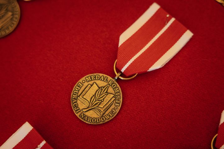Zdjęcie przedstawia Medal Komisji Edukacji Narodowej na czerwonym tle