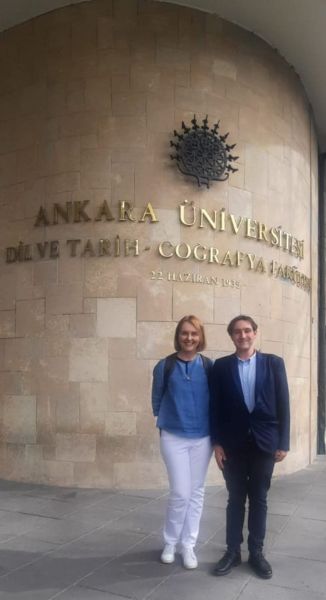 Prof. Romana Łapa wraz ze studentem z Turcji pozują przed ścianą z nazwą Uniwersytetu w Ankarze.