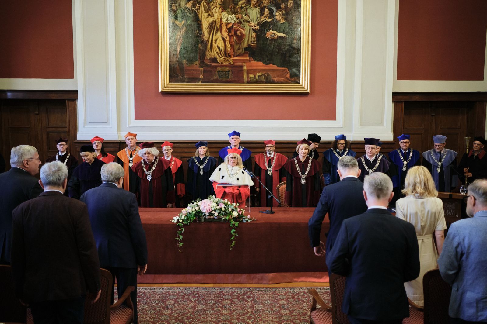 Stół prezydialny w Auli Lubrańskiego, za którym zasiadają Rektor i Prorektorzy oraz członkowie senatu UAM, wszyscy w odświętnych togach. Widać też część publiczności.