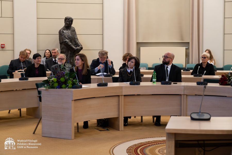 Uczestnicy jubileuszu siedzą za okrągłymi biurkami w Salonie Mickiewicza, z tyłu widać pomnik Adama Mickiewicza.