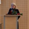 JM Rektor Bogumiła Kaniewska przemawia do mikrofonu, stojąc za mównicą, na której leży bukiet róż.